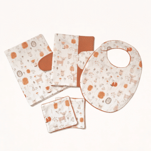 Ensemble d'accessoires de naissance en coton bio motif forêt avec pochette à langer, bavoir et protège carnet de santé sur une commode en bois.