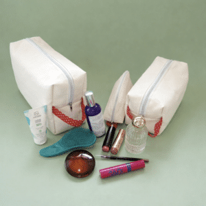 Vue d'ensemble des trois trousses (XL, grande et demi-lune) fermées, couleur sable avec anses rouges à pois blancs sur fond vert sauge.