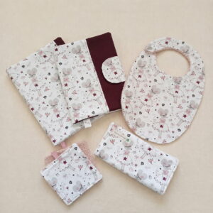 Un ensemble d'accessoires de naissance assortis pour bébé avec un motif de souris ballerine blanche et rose et du tissu bordeaux. L'ensemble comprend un protège-carnet de santé, un bavoir, une pochette à lingettes fermée et des carrés de coton lavables.
