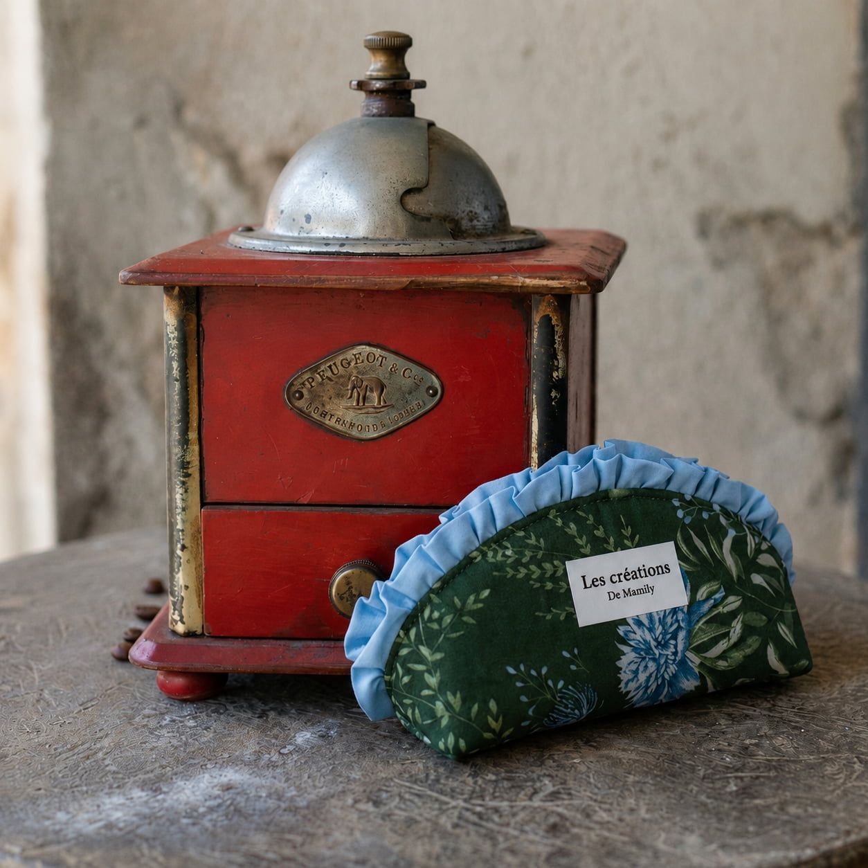 Ancien moulin à café Peugeot rouge et trousse en tissu faite main Les créations de Mamily sur une table en pierre.