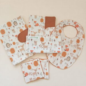 Ensemble de naissance de 6 pièces assorties avec un motif de la forêt (biches, renards, hiboux, écureuils). L'ensemble comprend un bavoir, un protège-carnet de santé, une débarbouillette, et des lingettes lavables, posés sur un tissu beige.