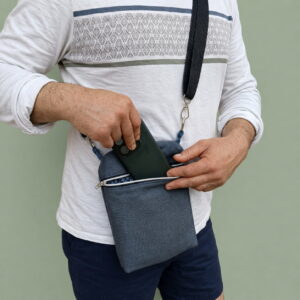 sacoche-homme-artisanale-canvas-gris-bleu (1) Sacoche homme en canvas gris bleu portée en bandoulière sur un t-shirt blanc.