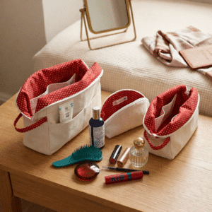Ensemble de 3 trousses de toilette artisanales en coton canvas beige avec doublure rouge à motifs cœurs, ouvertes sur une coiffeuse en bois.