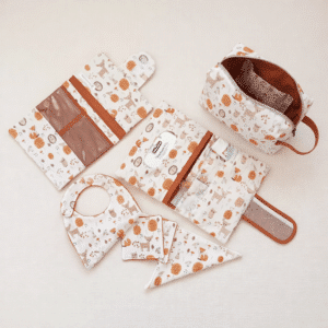 Ensemble d'accessoires bébé motif forêt avec trousse de toilette, bavoir et pochette nomade sur une table à langer.