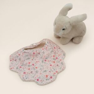 bavoir-bebe-fleurs-rose-peluche-lapin Bavoir bébé à motifs floraux roses avec peluche lapin sur fond beige uni.