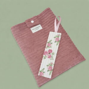 Vue à plat de l'ensemble Secret de Roses : pochette de livre en velours côtelé rose poudré et son marque-page assorti sur fond vert sauge.