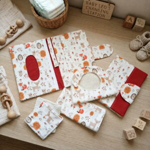 "Pochette à langer nomade ouverte et ses accessoires assortis motif animaux de la forêt, présentés sur une table à langer en bois avec des cubes et hochet pour bébé."