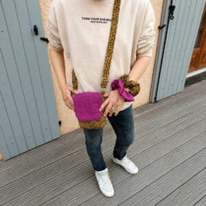 sacoche-bandouliere-leopard-fuchsia-femme-portee (1) Femme portant une sacoche bandoulière en tissu léopard avec rabat fuchsia et deux chouchous assortis au poignet.