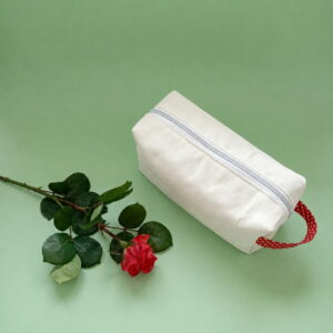 Trousse de toilette en coton épais crème avec fermeture éclair dorée et anse rouge à motifs.