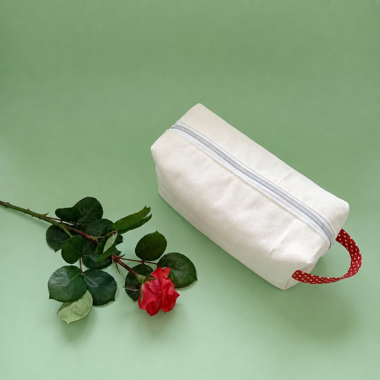 Trousse de toilette en coton épais crème avec fermeture éclair dorée et anse rouge à motifs.