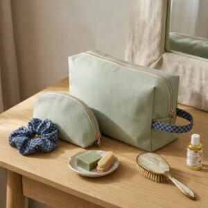Ensemble de deux trousses de toilette en coton vert sauge et chouchou bleu assorti posés sur une coiffeuse en bois.