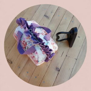 Vanity case artisanal en tissu imprimé fleurs et papillons avec volants violets sur fond uni rose poudré.